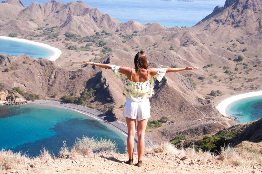 a girl standing on top of Padar island with her arms spread out viewing down on three beaches