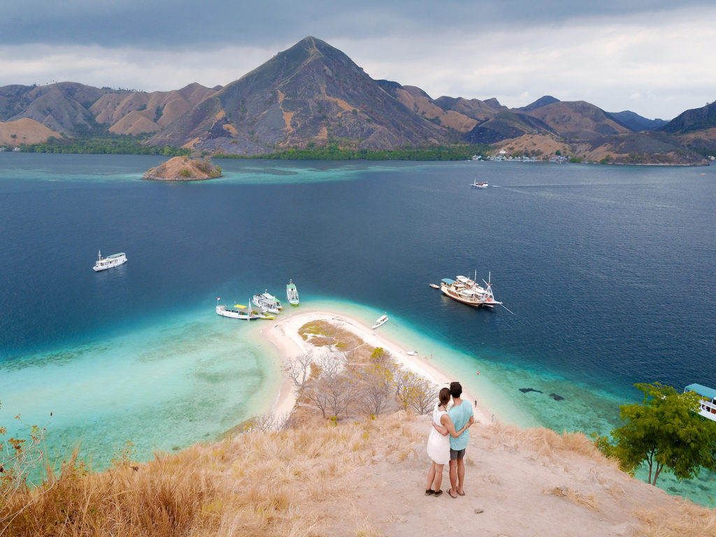 a drone shot of 2 people standing on top of kelor island enjoying the view on the surrounding islands and the ocean 