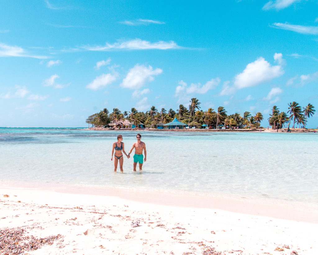 two people holding hands on white sand beach with perfect azure water on San Andres which is one of the most beautiful places in South America