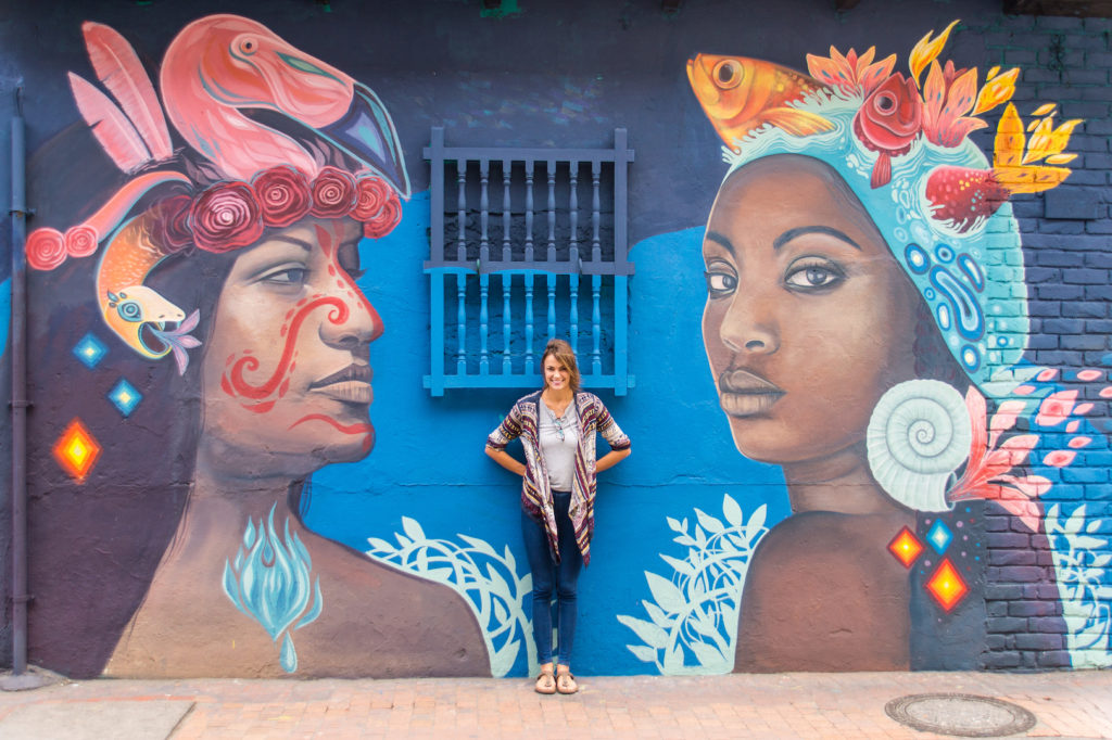 a pretty girl posing in front of a mural displaying two women in Bogota, Colombia