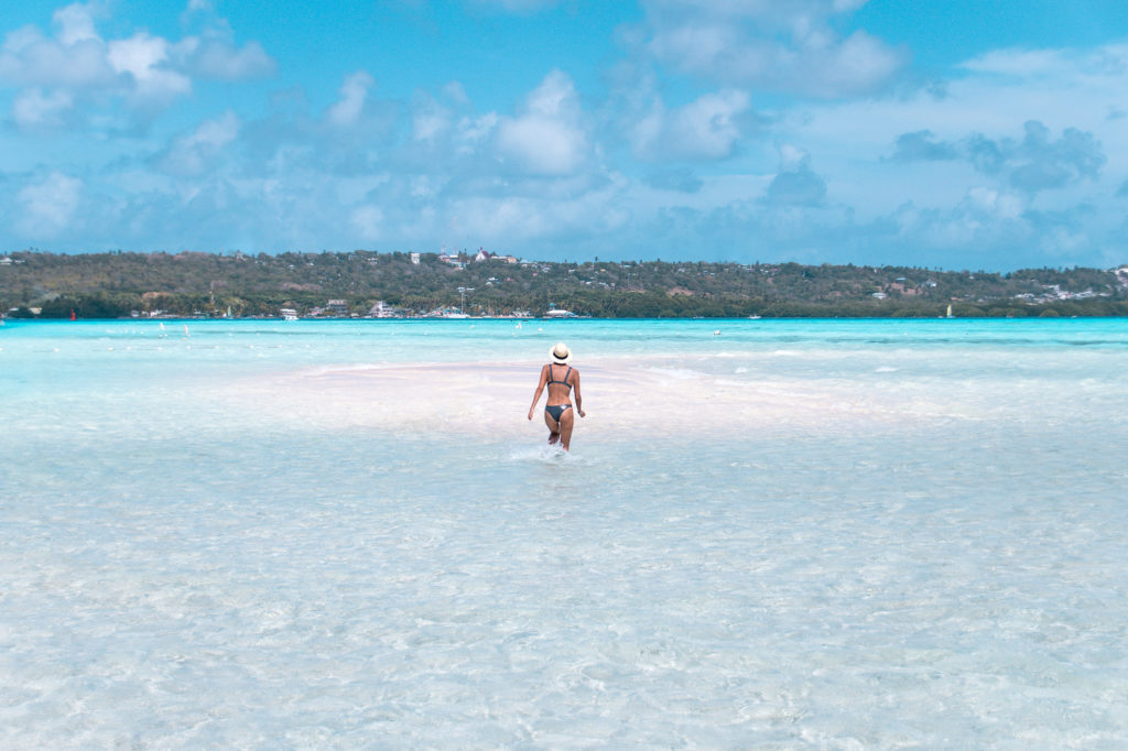 a woman in swimwear running in shallow water towards a sandbank