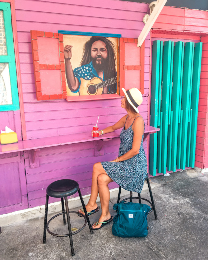 a woman sitting on a chair in front of a pink wooden hut drinking a coke