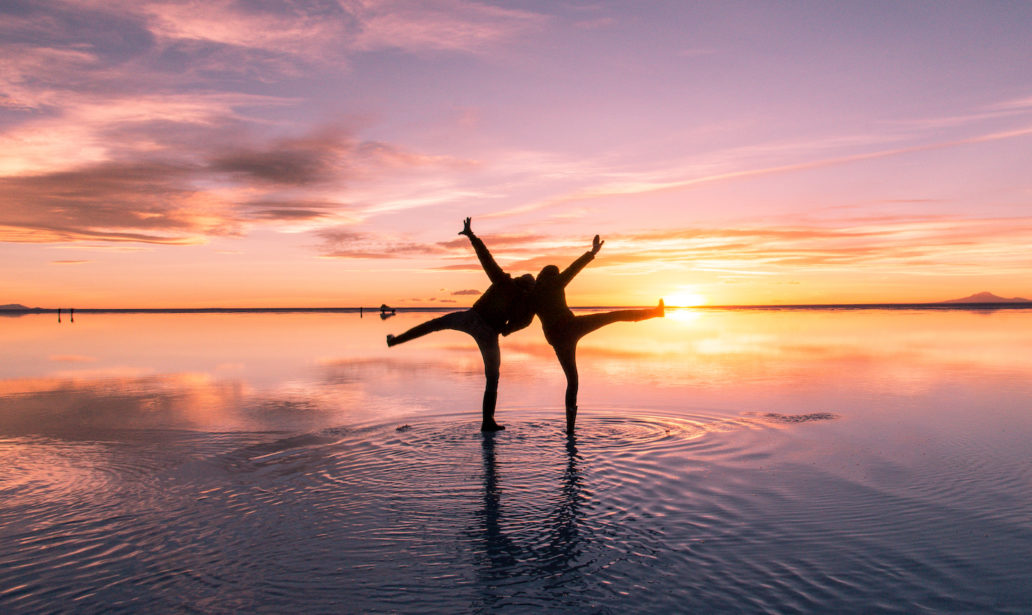 two people posing on salt flats during sunset colours and water reflection in Bolivia