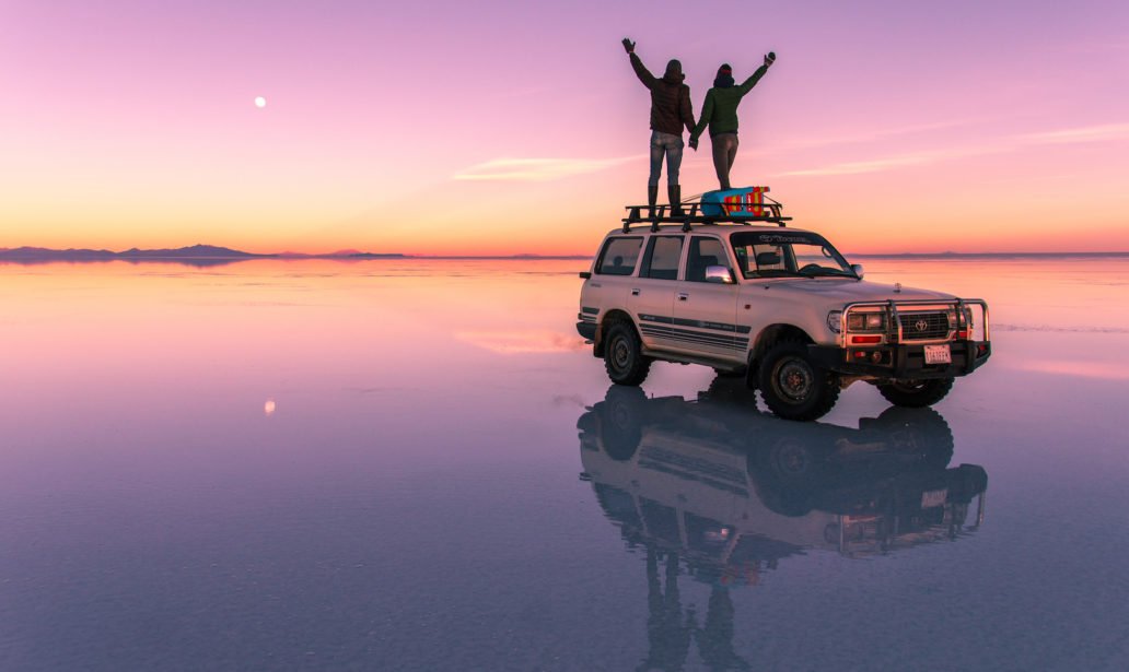 two people standing on the car and looking at the pink sunset colours in Salar de Uyuni.