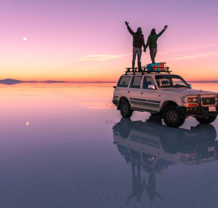 two people standing on the car and looking at the pink sunset colours in Salar de Uyuni.