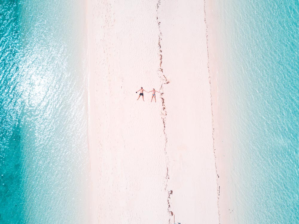 2 people lying on the longest sand bar surrounded by turquoise water