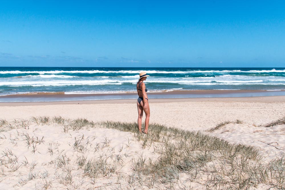 a girl in swimwear standing in sand dunes looking out on the ocean