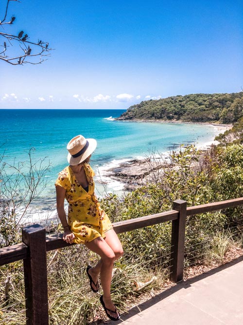 a girl wearing a yellow dress sitting on a hand rail and looking out on a bay in noosa national park