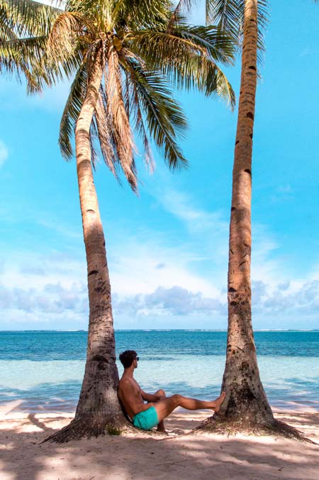 a boy in swimshorts sitting between two tall palm trees on Siargo during 2 weeks in the philippines