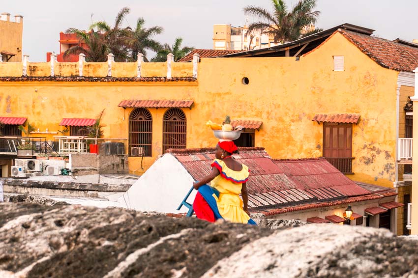 A view on the orange wall and woman from Cartagena walking with a fruit basket on her head