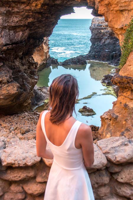 a woman standing in front of the cave with a view on the ocean