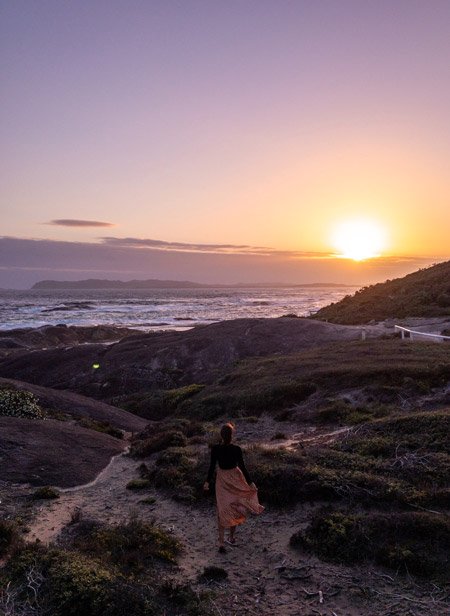A woman in a dress walking next to coastal flora during sunset
