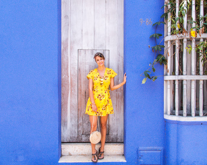 a woman in a yellow dress standing in front of the purple wall, white window and yellow flowers in Cartagena, Colombia