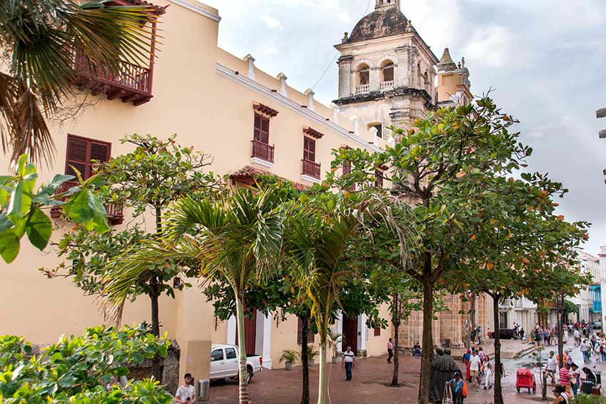 church and green trees with people walking on the plaza in Cartagena, Colombia