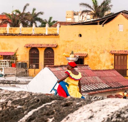 dreamy bucket list place called Cartagena, woman in a yellow dress walking in front of the orange building