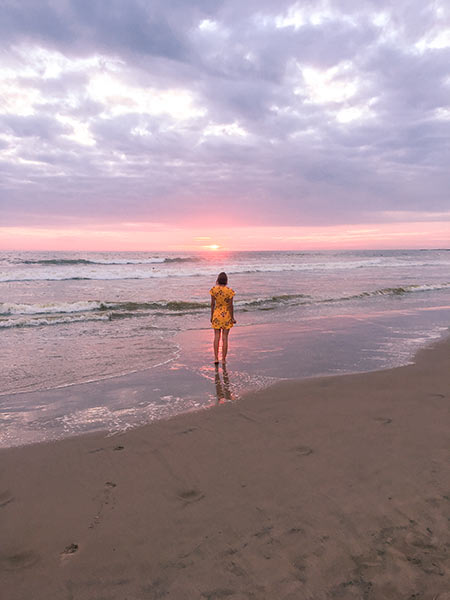woman in yellow dress looking out at the pink sky on Playa Montanita