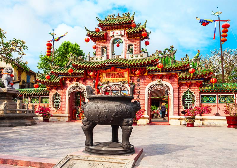 red Chinese temple with green plants, red lanterns and black vase praying statue.