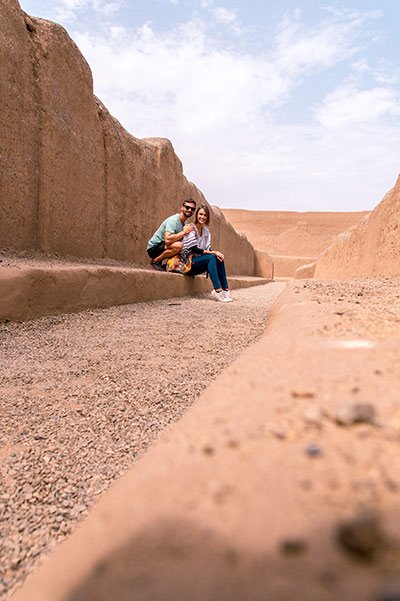 two people posing for a photo, sitting on the ground in front of the brown wall
