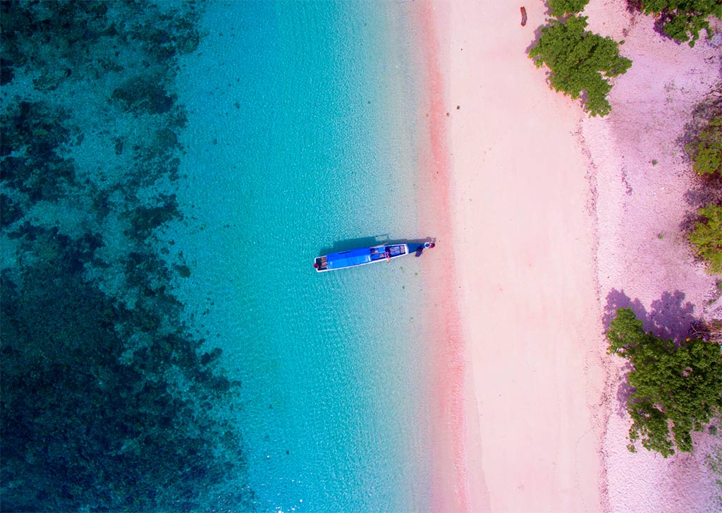 an arial view on the pink beach in Indonesia near Labuan Bajo, with a boat and turquoise water