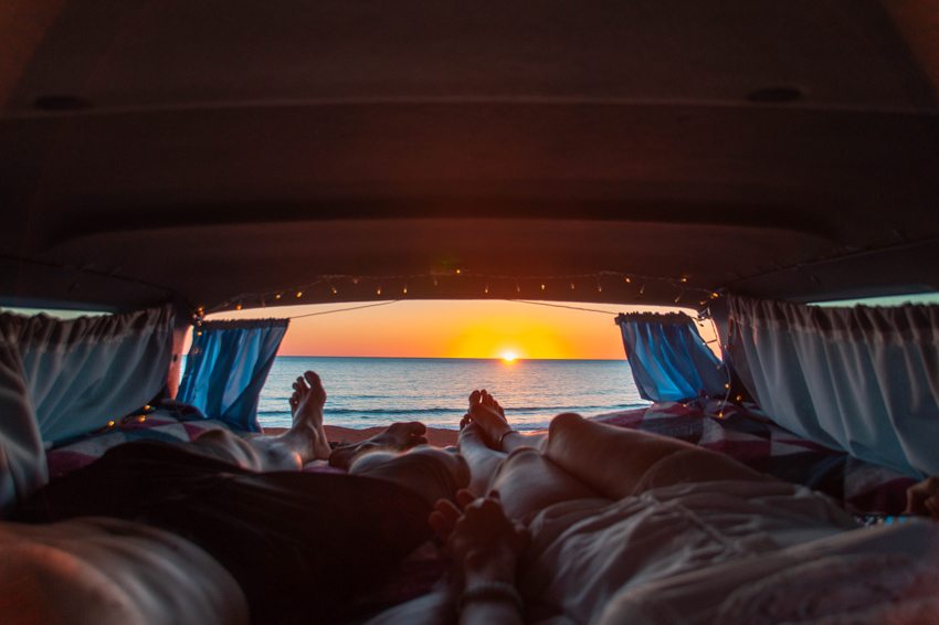 two people laying in the camping van and watching sunset